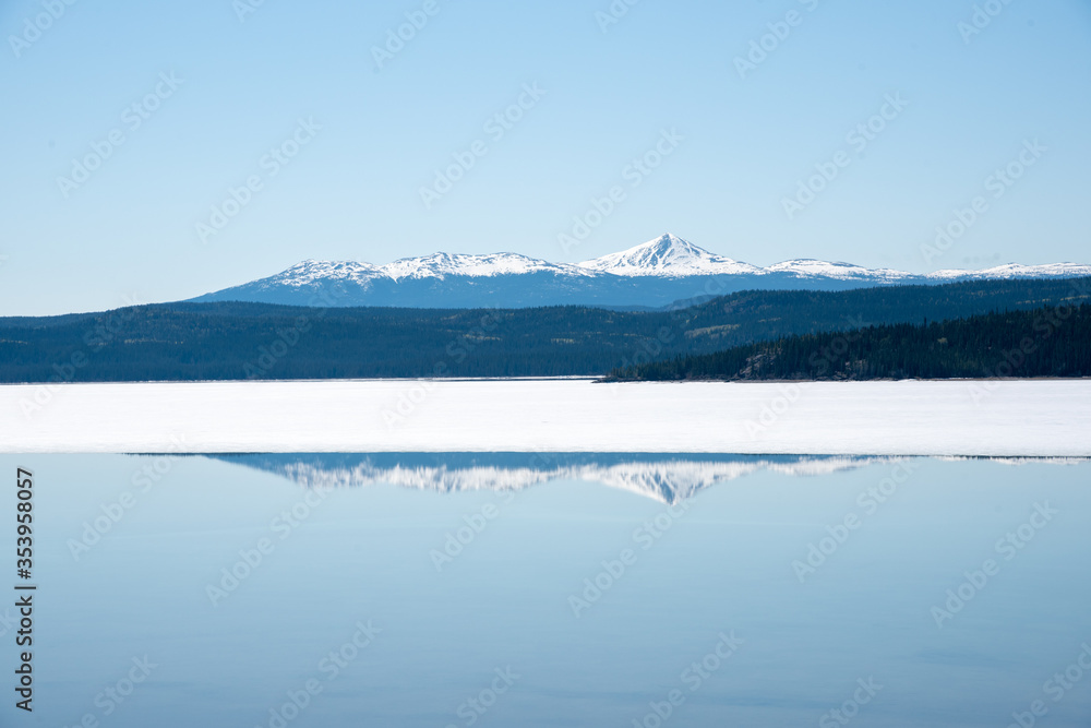 Pristine and calm lake in Yukon Territory with amazing reflection on blue sky day with snow capped mountains in spring time. 