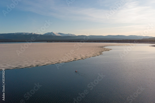 Sunset drone aerial view of person kayaking on blue pristine, stunning lake in northern Canada with ice. 