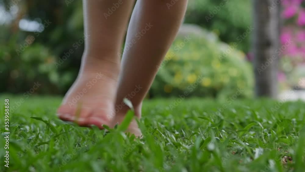 Closeup little girl playing outdoors runs on bright green beautiful grass with yellow flowers, outdoors at high angle feet of a small child who runs on the lawn near the house. Closeup little girl playing outdoors runs on bright green beautiful grass with yellow flowers, outdoors at high angle feet of a small child who runs on the lawn near the house.
