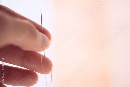 Fotografija needle with a pink thread in a female fingers