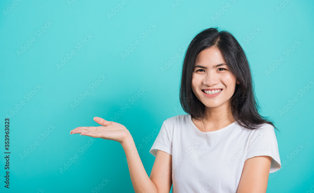 Portrait Asian beautiful young woman standing wear t-shirt, She showing hand to presenting product and looking at the camera, shoot photo in a studio on blue background, There was copy space Portrait Asian beautiful young woman standing wear t-shirt, She showing hand to presenting product and looking at the camera, shoot photo in a studio on blue background, There was copy space