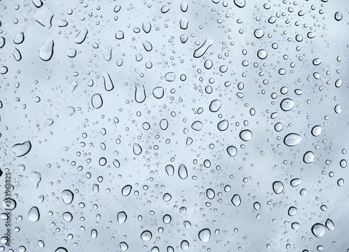 Raindrops on a transparent glass against a cloudy blue sky. Condensation and precipitation concept.