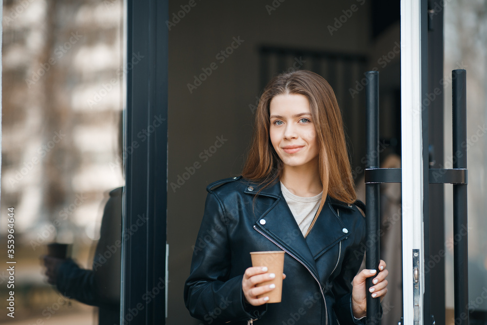 Young cute girl open the door of cafe and holding coffee