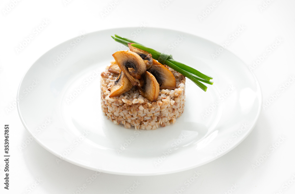 Buckwheat porridge with mushrooms, garnish in a plate on the table. Isolate
