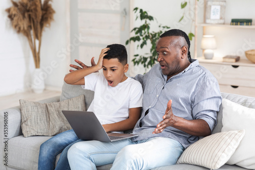 African boy and his grandfather looking at laptop screen with shock