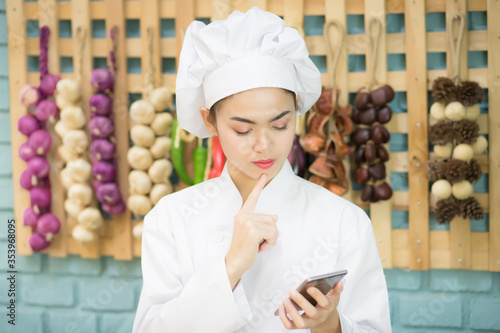 Beautiful Asian Asian chefs are looking for a mobile phone in a kitchen full of spices in the concept of ordering food through an application on a smartphone.