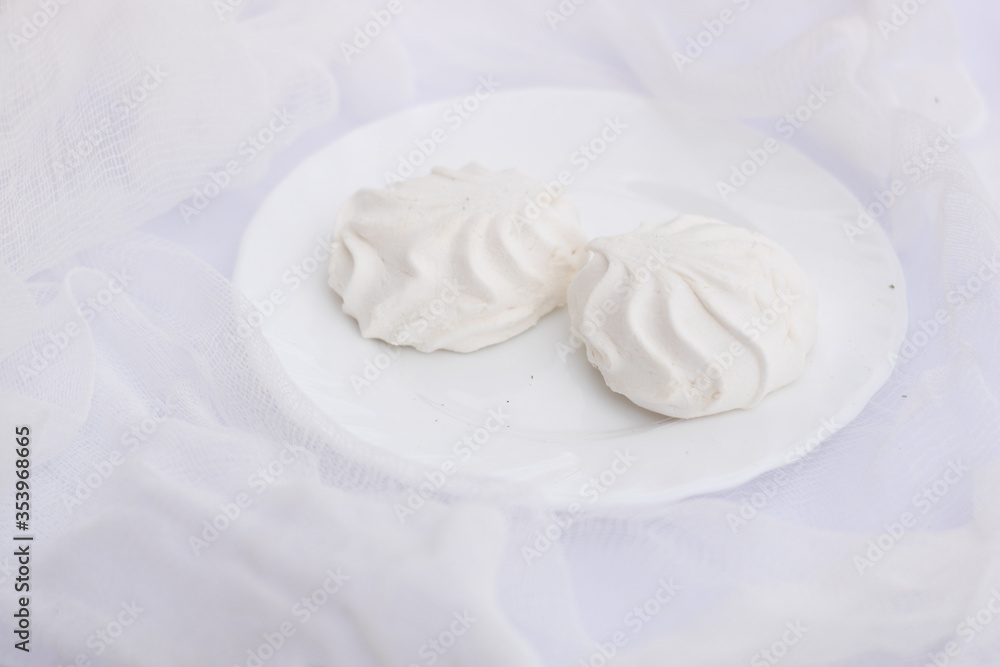Two white wavy marshmallows zephyr lying on plate on airy snow white cloth