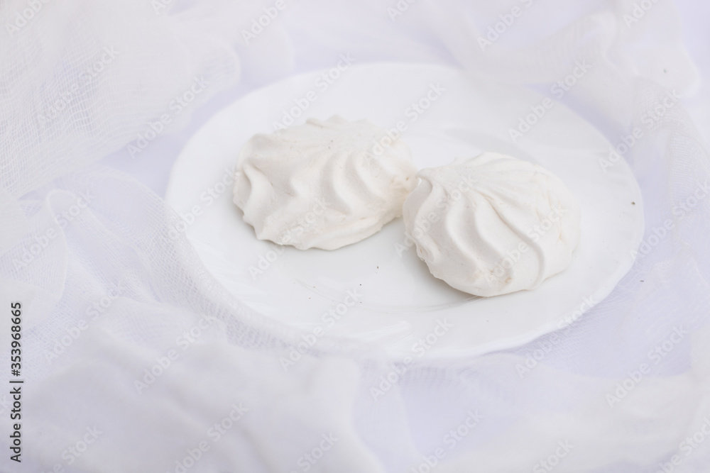 Two white wavy marshmallows zephyr lying on plate on airy snow white cloth Two white wavy marshmallows zephyr lying on plate on airy snow white cloth