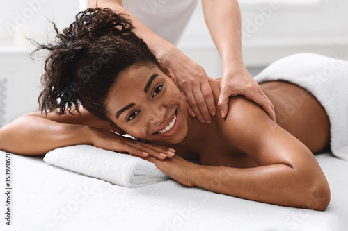 Happy african girl enjoying back massage at spa