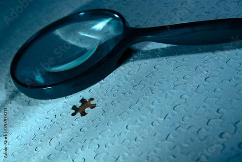 Jigsaw puzzle with missing piece and an investigator's magnifying glass in blue ambient hue.