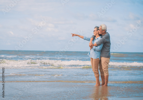 Side view of romantic senior couple while standing hugging each other while at beach and pointing hands forward. image not focus..Retirement age concept and love, copy space for text