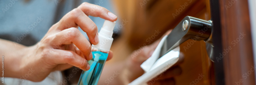 woman hand disinfecting the door handle by spraying a blue sanitizer from a bottle for Covid-19 Coronavirus prevention. - obrazy, fototapety, plakaty 