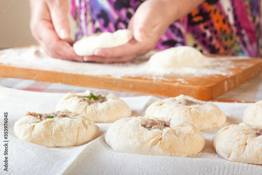 Raw dough with meat filling on the table against the background of female hands with pieces of dough.
