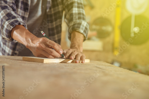 Carpenter working on woodworking machines in carpentry shop. Asian craftsman works in a workplace. Cabinet maker at the table with pencil drawing sign on plank