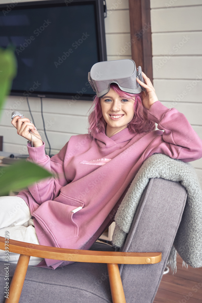 Happy hipster teen girl pink hair wear vr glasses headset hold controller  sit in chair look at camera. Digital innovation video game, virtual reality  3D 360 video app entertainment. Vertical portrait foto