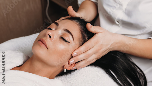 Close up photo of a head massage session done to a young brunette woman with closed eyes at the spa salon
