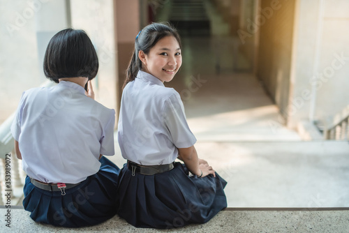 A pretty Asian female student in white uniform is sitting and turning her face and smiling on the school stair.