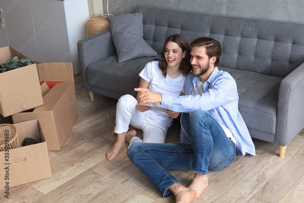 Happy couple sitting and planning new home decoration at home with a tablet at moving day, renovation and interior design for new house Happy couple sitting and planning new home decoration at home with a tablet at moving day, renovation and interior design for new house