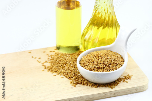 flax seeds in white bowl and bottle of flaxseed oil on wooden board
