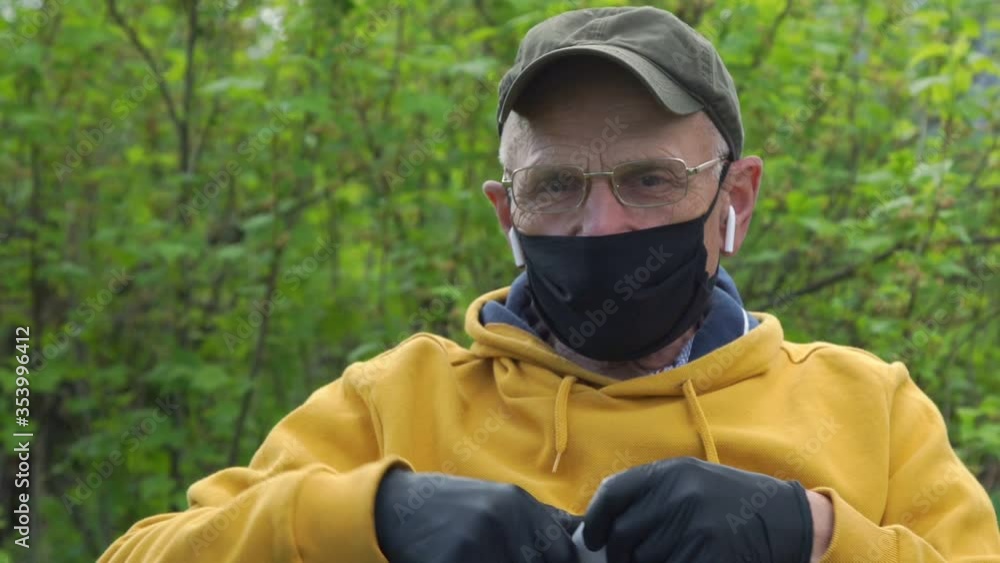 senior man in mask and gloves checks sound of wireless headphones sitting in garden and talking with friend closeup senior man in mask and gloves checks sound of wireless headphones sitting in garden and talking with friend closeup