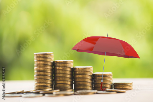 Red umbrella protects rows of increasing coins on table. Concept long term money investment and wealth management with risk protection, financial depicts securing asset for sustainable growth