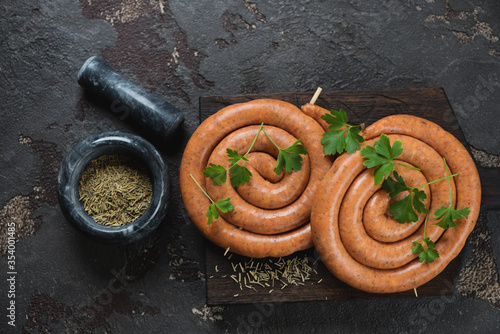 Raw pork coiled sausages and seasonings over brown stone background, view from above, horizontal shot