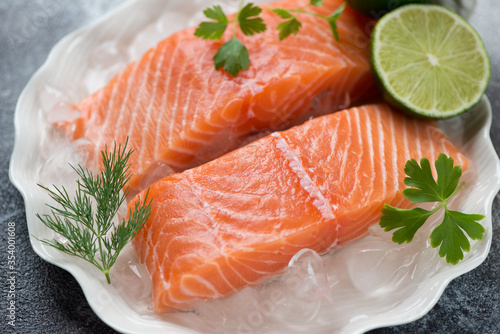 Close-up of raw iced slices of salmon fillet with fresh parsley, dill and lime, selective focus