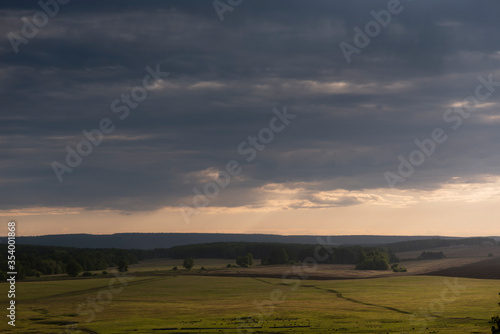 Plowed field with soil chernozem before sowing against the backdrop of a beautiful sunset with clouds. Landscape. View from the hill.