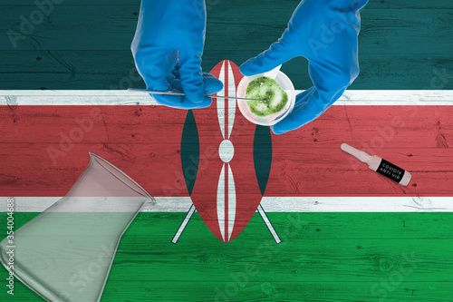 Kenya flag on laboratory table. Medical healthcare technologist holding COVID-19 swab collection kit, wearing blue protective gloves, epidemic concept.
