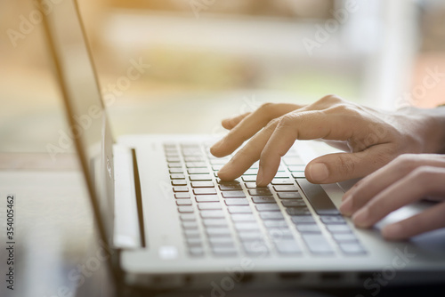 Close up of businesswoman hands typing on laptop keyboard with smart phone and coffee beside on a wooden table in coffee shop.Typing on keyboard.Warm sunlight.