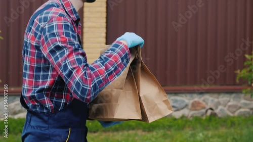 Side view: A man wearing a mask and gloves carries bags of groceries to the customer's house photo