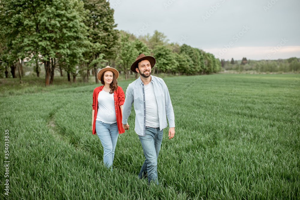 Pregnant woman with her man having fun together, walking on the greenfield. Happy couple expecting a baby, young family concept Pregnant woman with her man having fun together, walking on the greenfield. Happy couple expecting a baby, young family concept