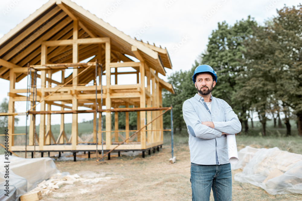 Portrait of an architect or builder with blueprints on the construction site outdoors. The concept of building and designing a wooden frame house