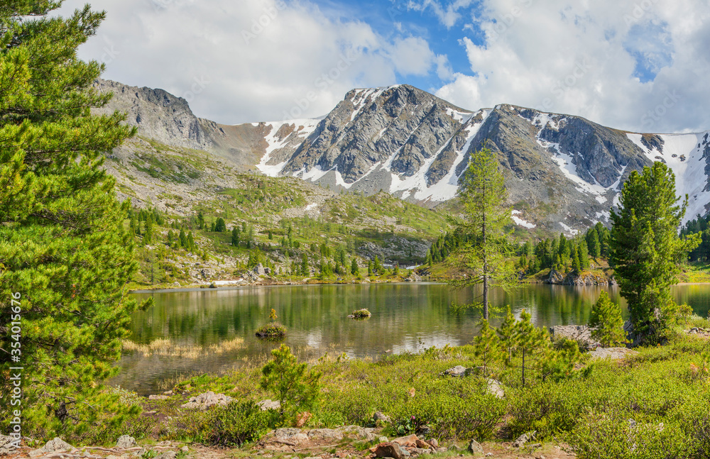Fototapeta premium Mountain landscape, picturesque mountain lake in the summer morning, Altai. Trees on the shore, snow on the slope.
