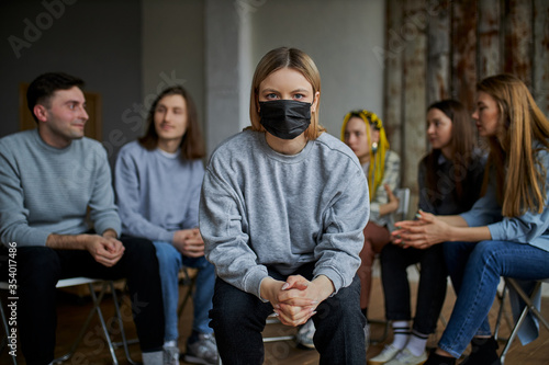 young caucasian woman wearing mask sitting in a distance from other people, keep distance protect others from COVID-19 viruses, epidemic