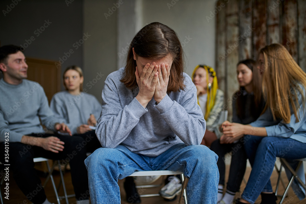 young male suffer from alcohol addiction, cry, sit apart from group of people gathered in the club of anonymous alcoholics young male suffer from alcohol addiction, cry, sit apart from group of people gathered in the club of anonymous alcoholics