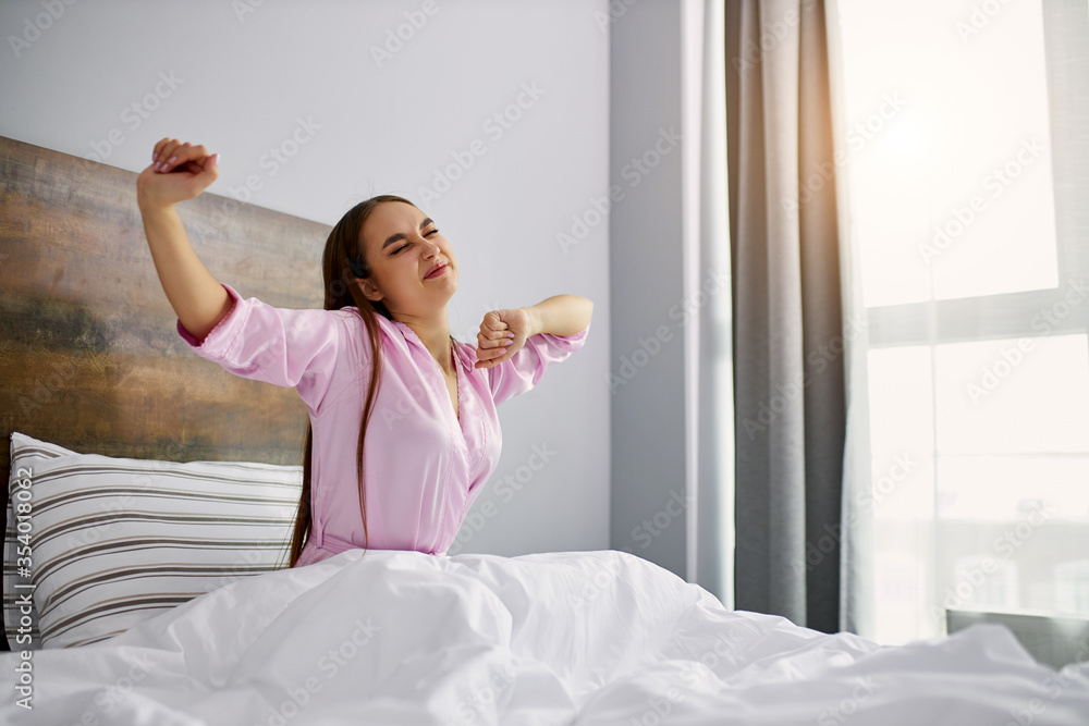 sweet sleepy caucasian woman is stretching on bed, woman just woke up. she is in pajamas. in light bedroom sweet sleepy caucasian woman is stretching on bed, woman just woke up. she is in pajamas. in light bedroom