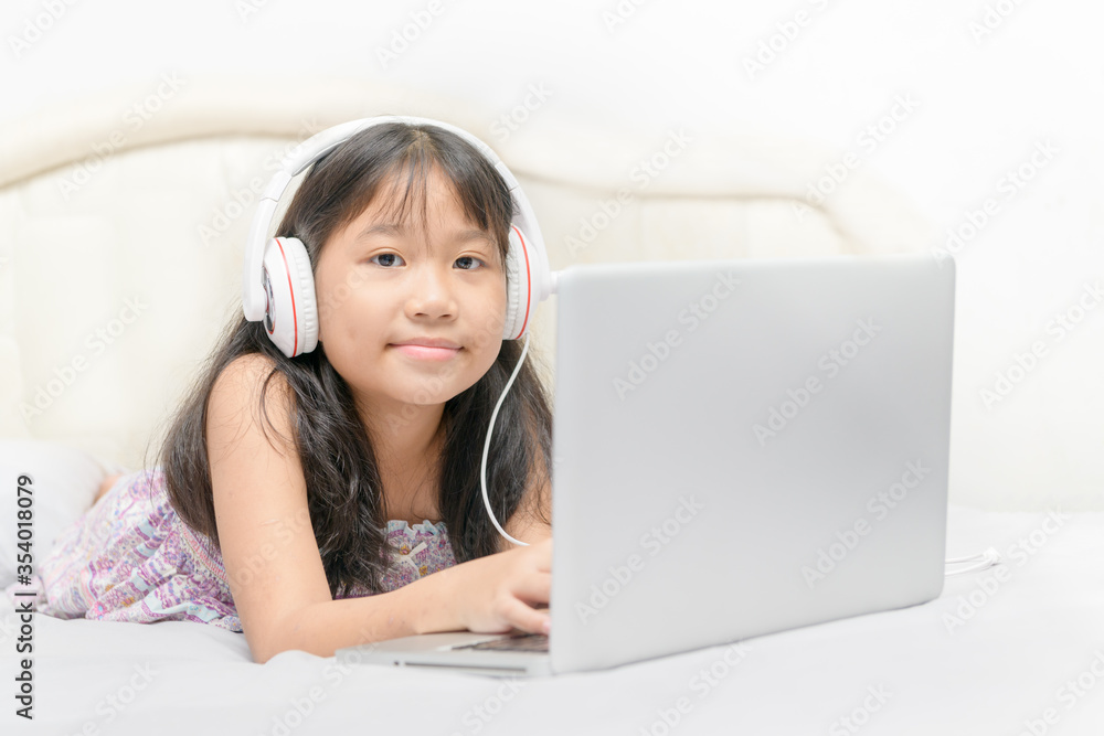 Happy cute girl lying and wearing headphones to learn online from a laptop Happy cute girl lying and wearing headphones to learn online from a laptop