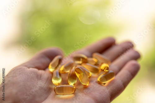 A handful of vitamin d capsules is in a man's hand. Blurred background of greenery