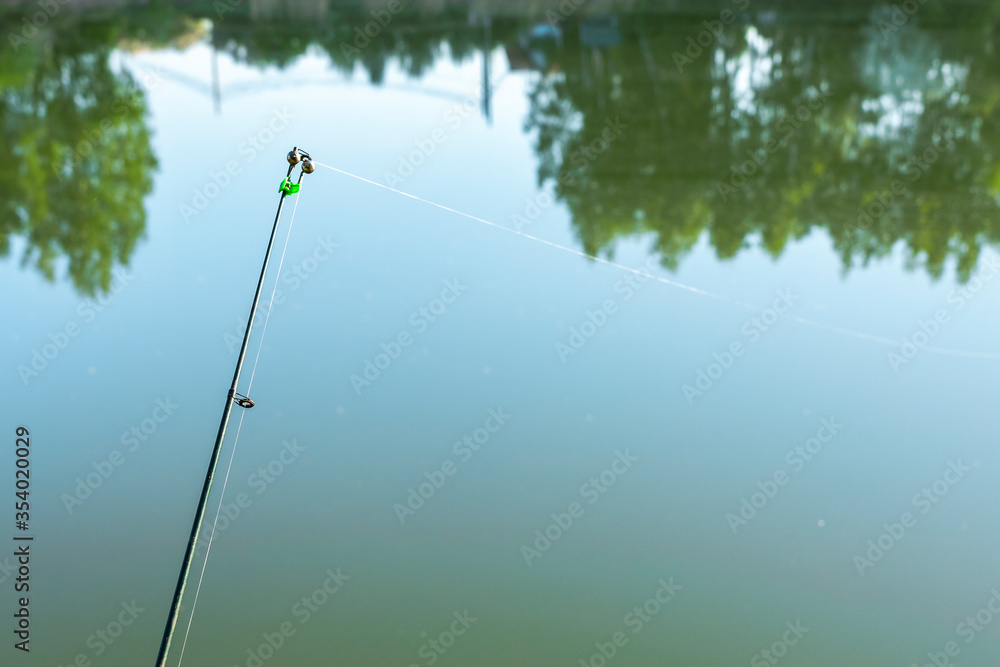 Bell on a fishing rod on the background of the river close-up. Summer fishing