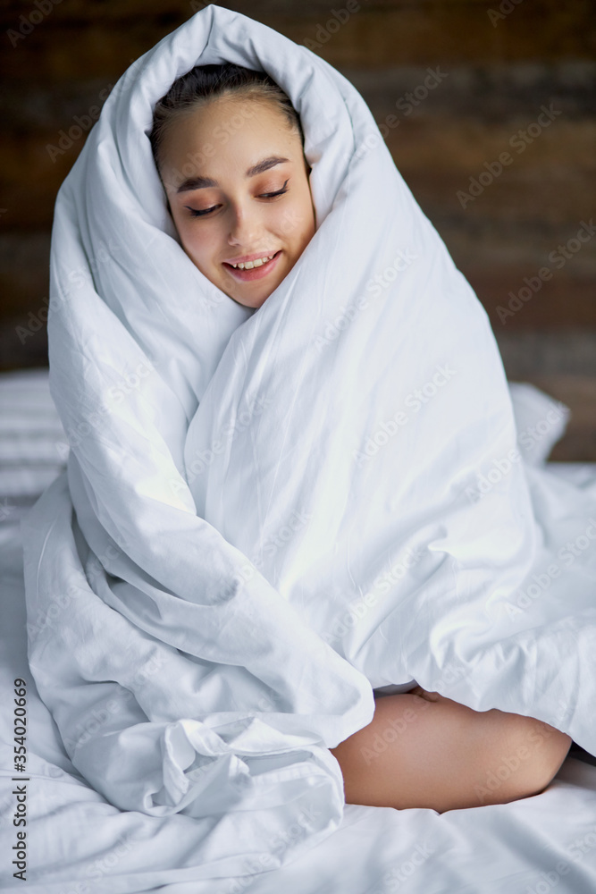 funny young woman is wrapped in blanket on bed, sits in the morning, doesn't want to wake up funny young woman is wrapped in blanket on bed, sits in the morning, doesn't want to wake up