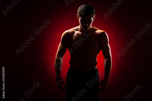 Athletic man. Guy without a T-shirt on a dark background. Concept - guy fitness model. Inflated guy stands in the dark. Male athlete. Man posing shirtless. Concept - trainer in a fitness club.