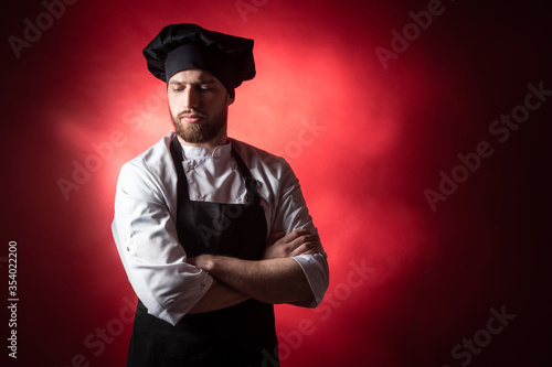 Cook guy. Chef with folded arms. Cook with folded arms on a dark background. Portrait of a pensive chef with his arms crossed. Restaurant chef was thinking about something. Man in a cook uniform