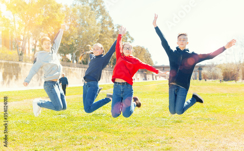 Four joyful teens jump on a lawn