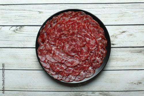 Ration of acorn-fed iberian sausage on black plate on rustic wooden table top view