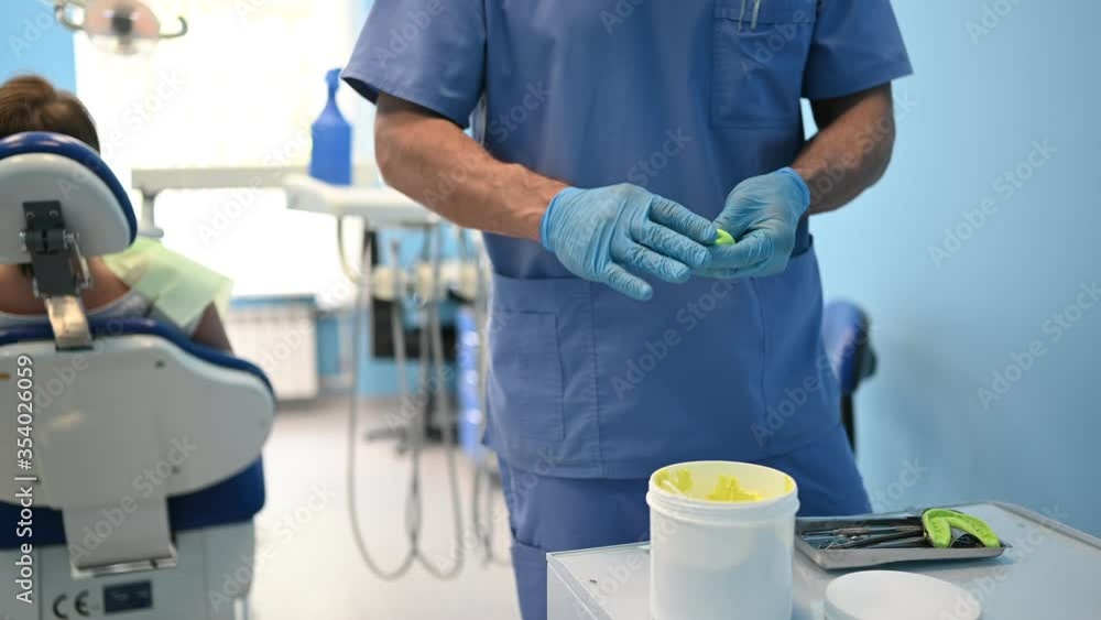 Doctor dentist in medical blue uniform makes a plaster or silicone material cast of set of teeth using dental equipment in dentistry office. Stomatology and health care concept. Doctor dentist in medical blue uniform makes a plaster or silicone material cast of set of teeth using dental equipment in dentistry office. Stomatology and health care concept.