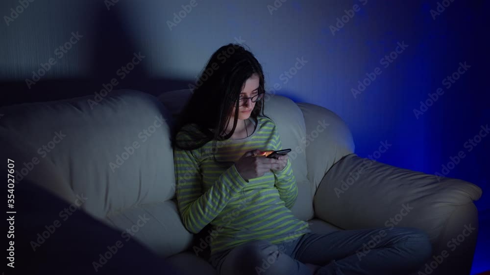 Cute teen girl in glasses sitting on the couch with his legs crossed and reading a conversation on your phone Cute teen girl in glasses sitting on the couch with his legs crossed and reading a conversation on your phone