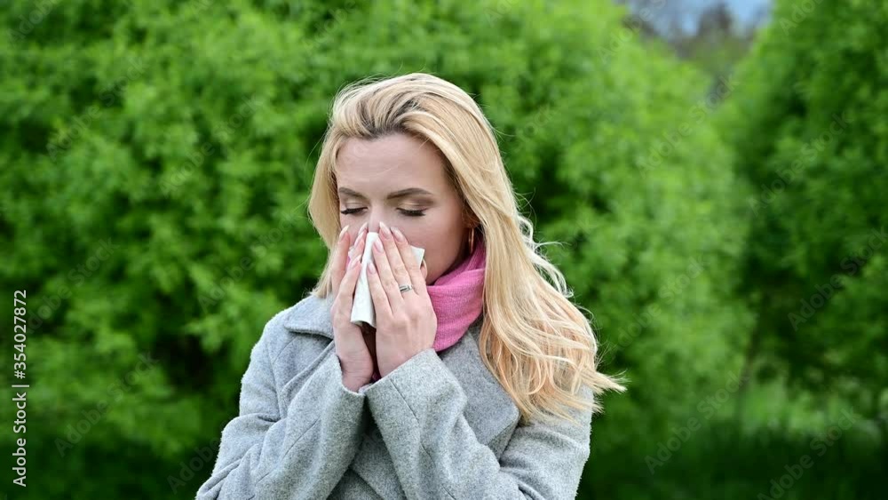 Video of a young caucasian pretty woman with a runny nose in an outdoor park. Model is wearing a coat in spring. Video of a young caucasian pretty woman with a runny nose in an outdoor park. Model is wearing a coat in spring.