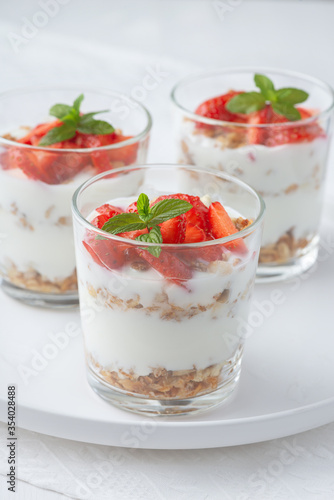  yoghurt with granola and strawberries in glass on a white table