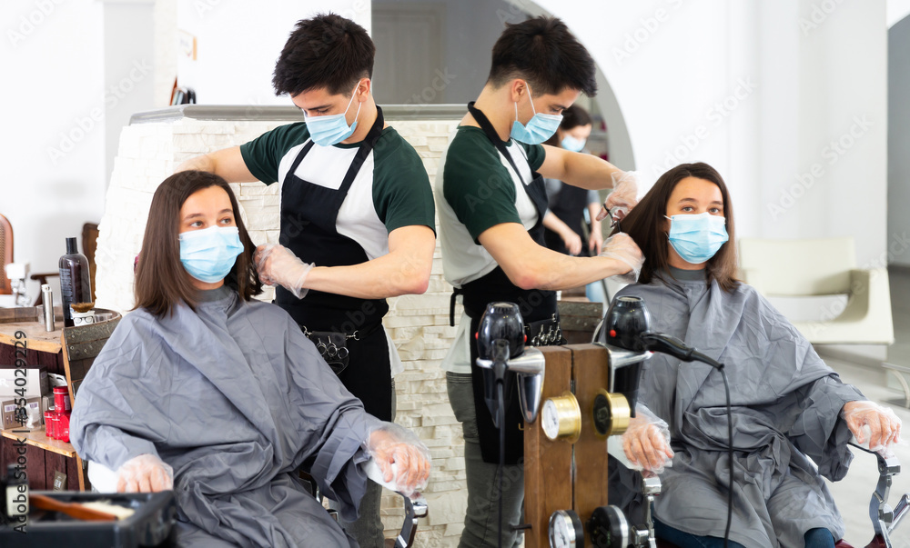 Fototapeta premium Young man professional hairdresser in mask cut female's hair